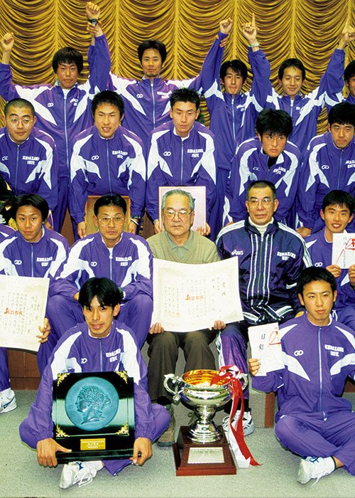 '00年優勝後の表彰式で記念写真。ジャージのデザインや会場の雰囲気に時代を感じる。コーチだった大八木（2列目左から3番目）は41歳